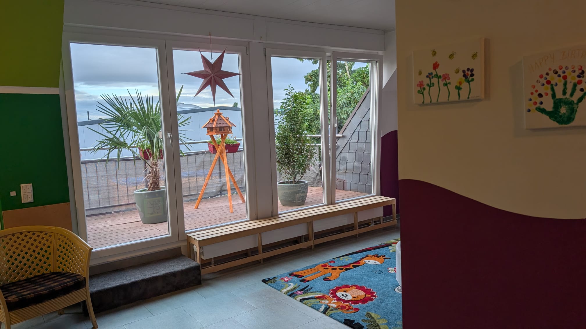 Spielbereich mit großer Fensterfront, kindgerechter Wandgestaltung und Spielteppich